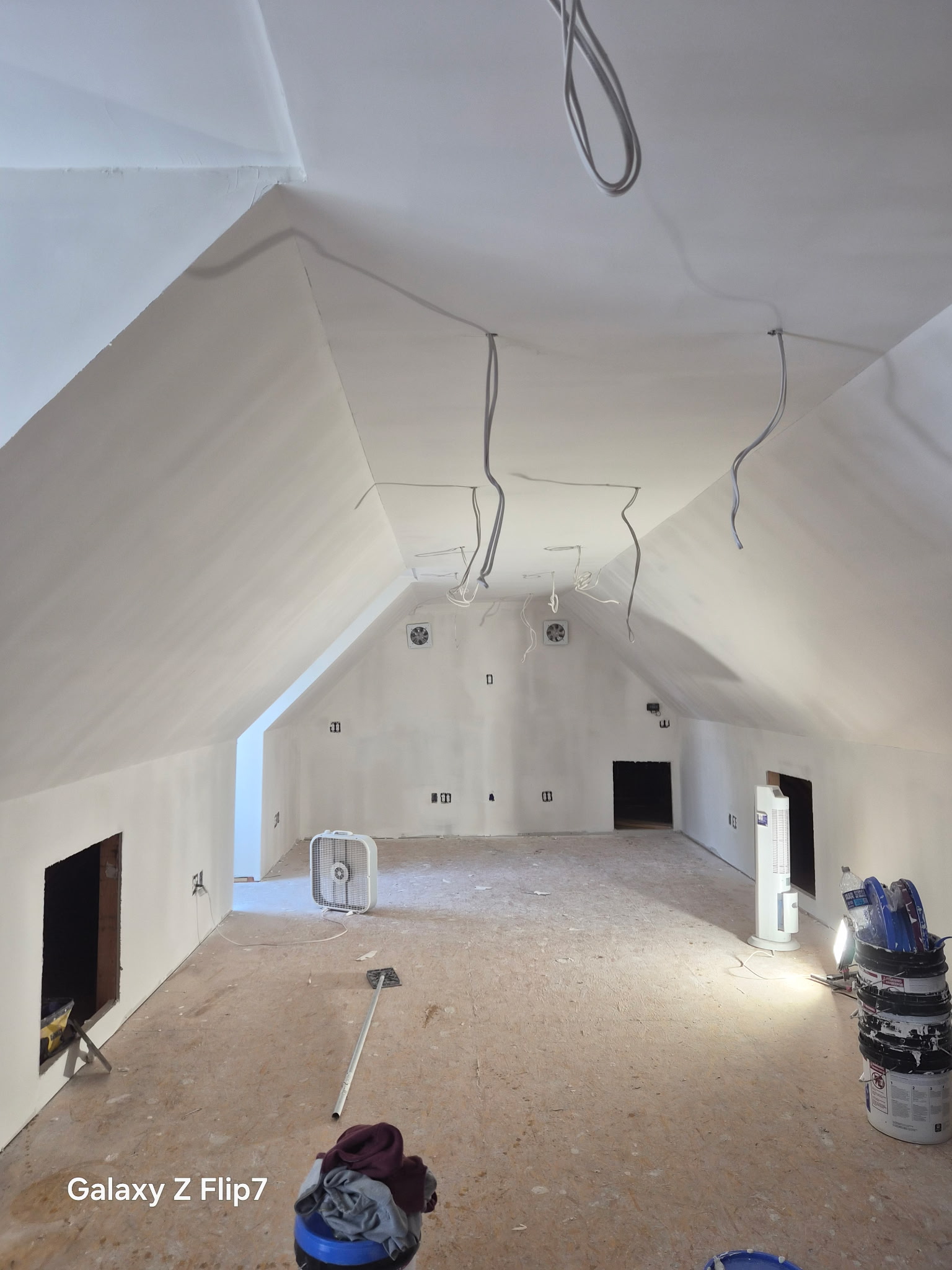Unfinished attic room with sloped ceiling, exposed wires, tools, and construction materials on the floor.