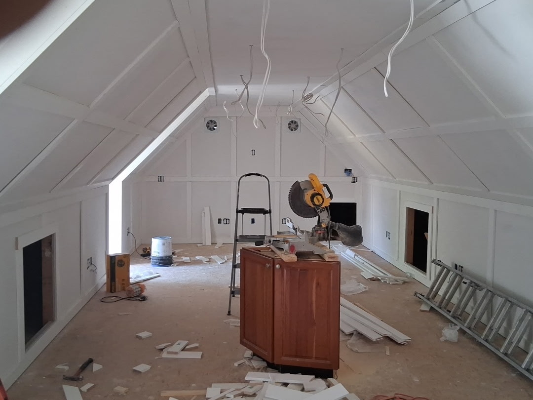 Unfinished attic room under construction, with tools, wood pieces, and a saw on a cabinet in the center.