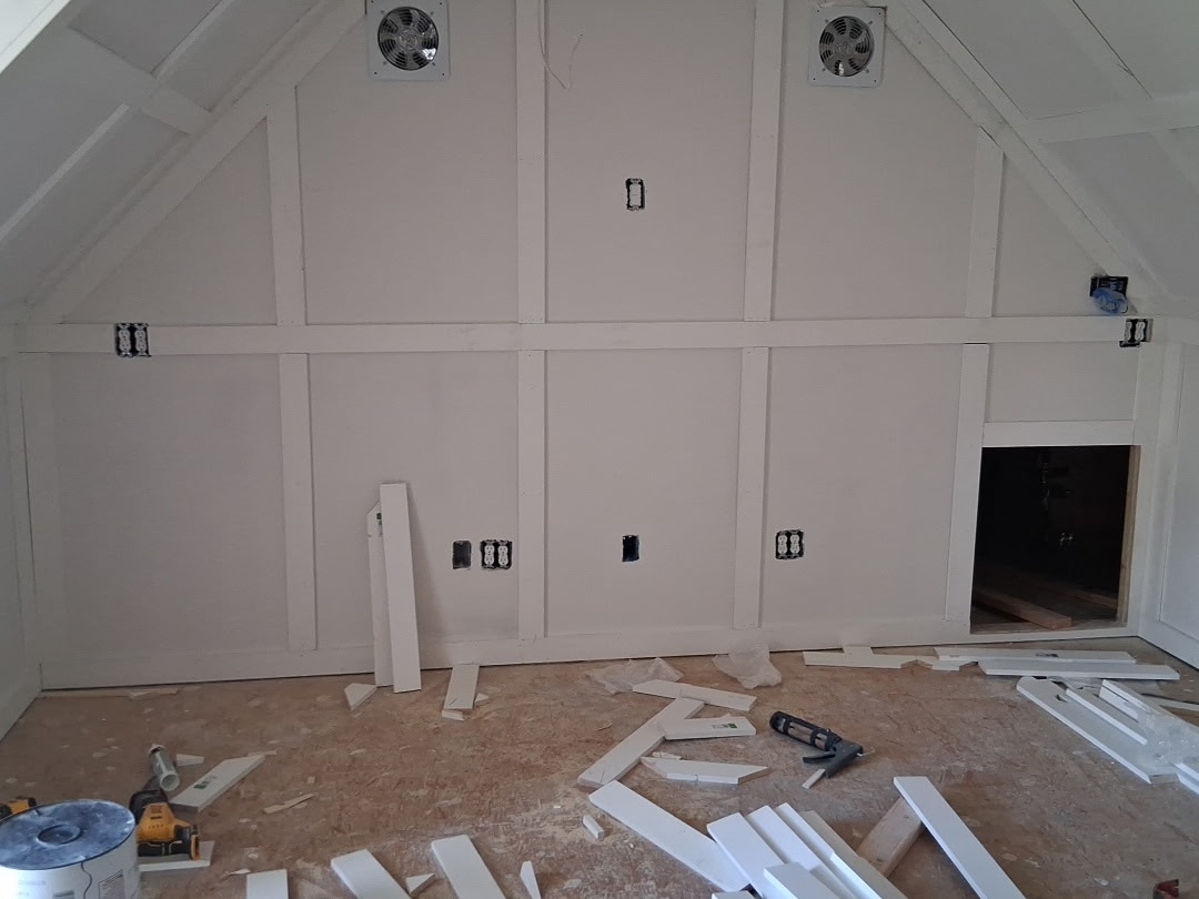 Unfinished attic room with white walls, construction tools, and wood pieces scattered on the floor.