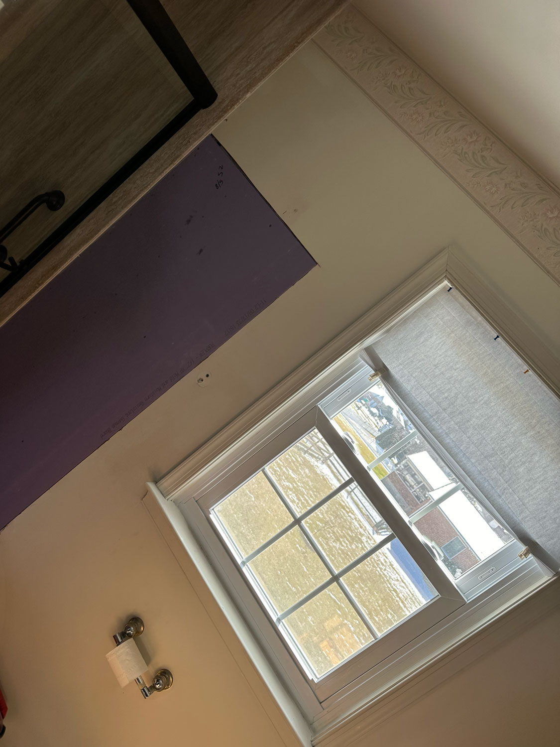 Bathroom window with a shade half-drawn, a partial purple wall, and a toilet paper holder on the left.