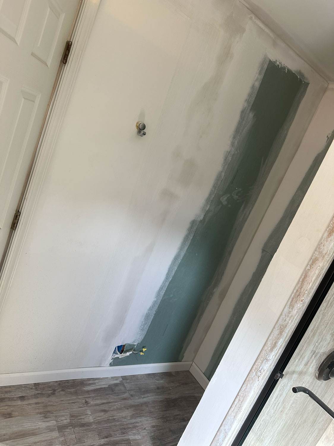 A partially finished wall with drywall and joint compound next to a door on a wood-patterned floor.