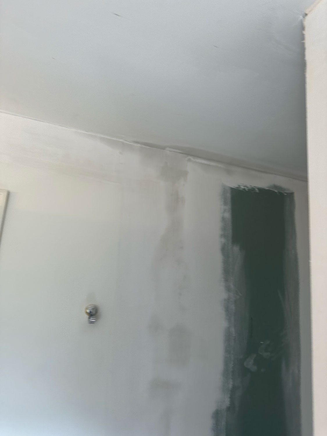 Partially painted wall with visible drywall seams and a single wall-mounted light fixture.