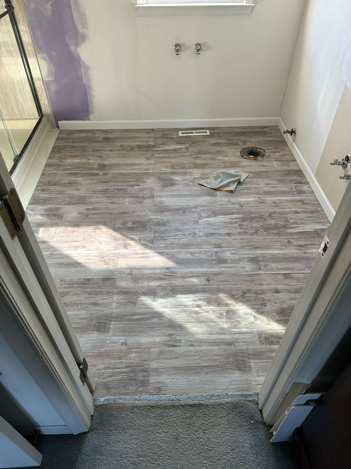 View of a small room with new wood-look vinyl flooring, plumbing fixtures, and unfinished walls.