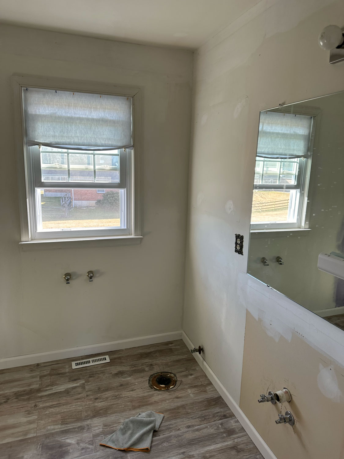 Partially renovated bathroom with exposed plumbing, empty floor, and a window letting in natural light.