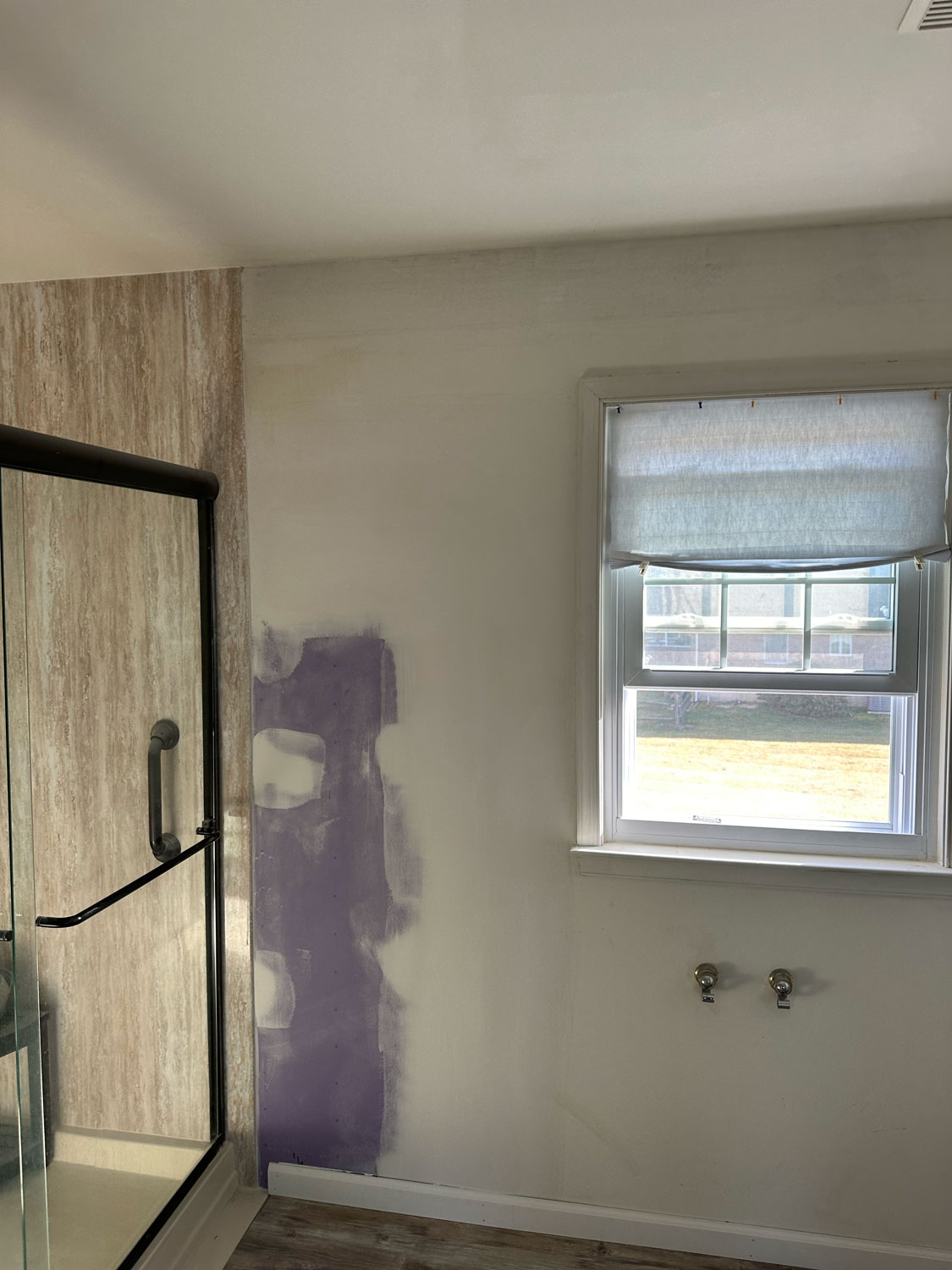 Bathroom under renovation with exposed drywall, missing sink, and a window with a shade partially drawn.