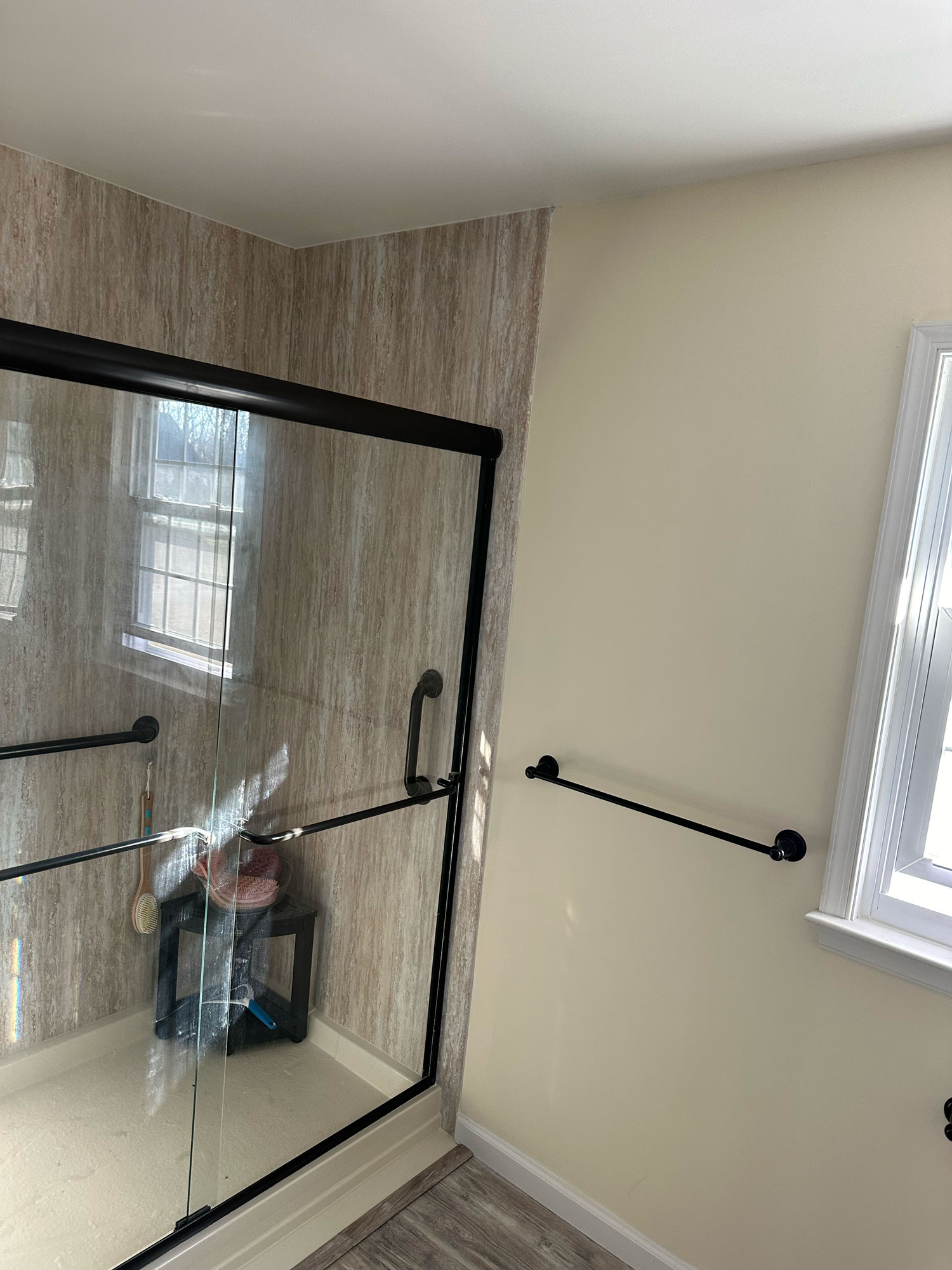 Shower with glass sliding doors next to a window and towel bar in a sunlit bathroom.