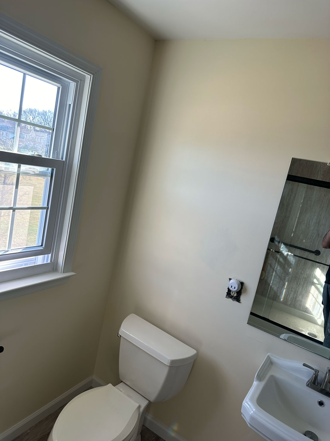 A small bathroom with a toilet, sink, mirror, and a window letting in natural light.