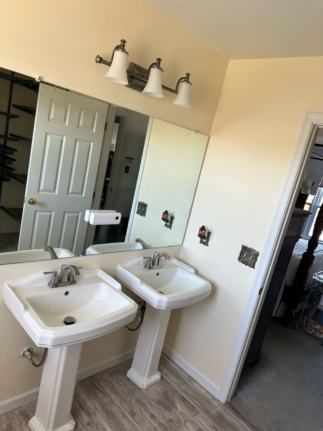 Two white pedestal sinks under a large mirror in a bathroom with unfinished wall outlets.