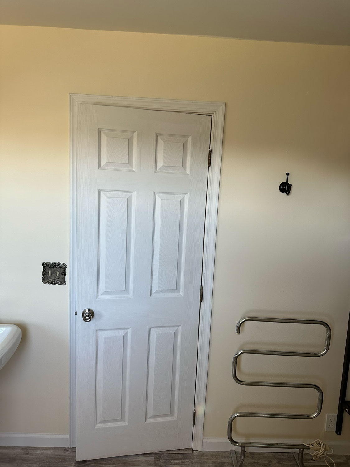 A white door in a beige room with a towel rack, wall hook, and a missing light switch plate.