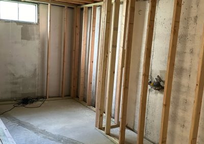 Partially finished basement room with exposed wooden framing and concrete walls under a small window.