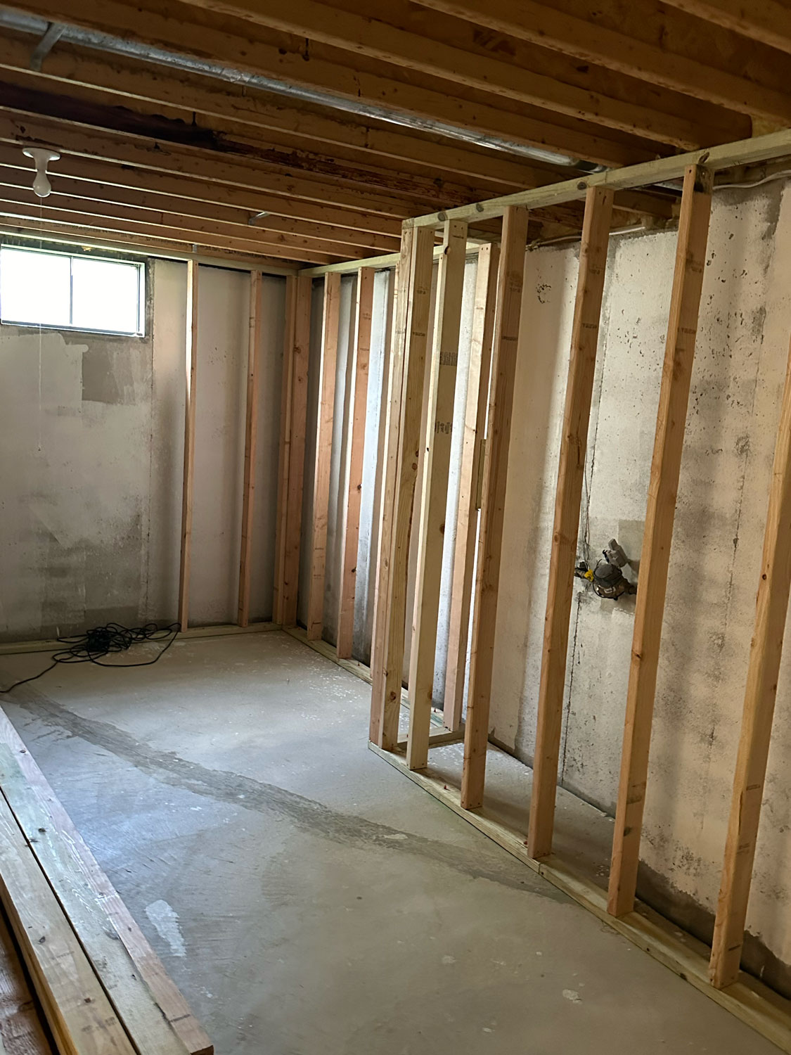 Partially finished basement room with exposed wooden framing and concrete walls under a small window.