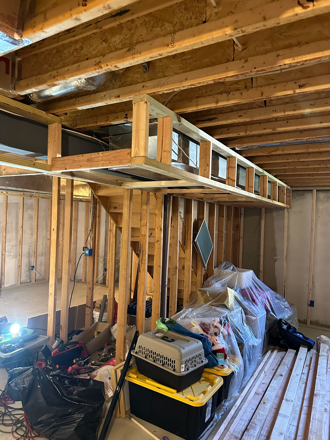 Partially finished basement with exposed wooden framing, storage bins, and construction materials scattered around.