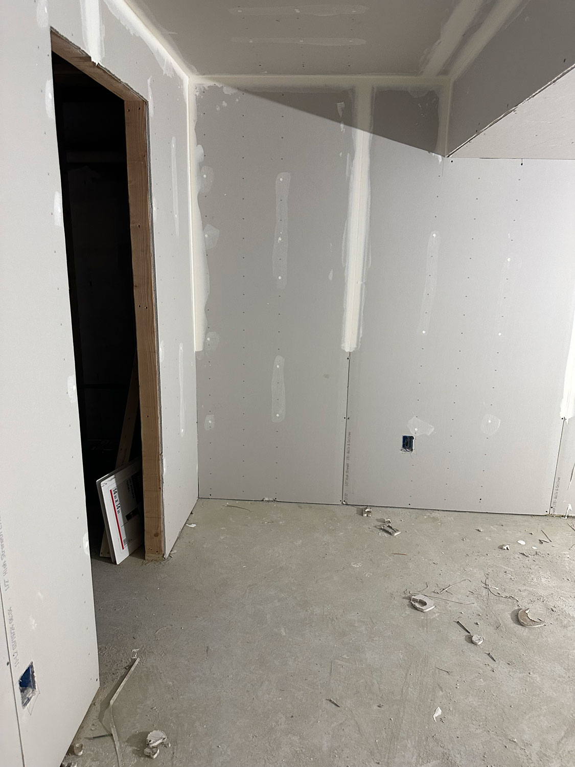 Room under construction with unfinished drywall, exposed joints, and a partially open doorway on the left.