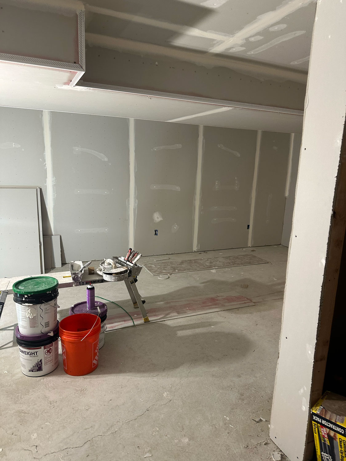 Room under construction with unfinished drywall, paint cans, and supplies on a sawhorse and the floor.
