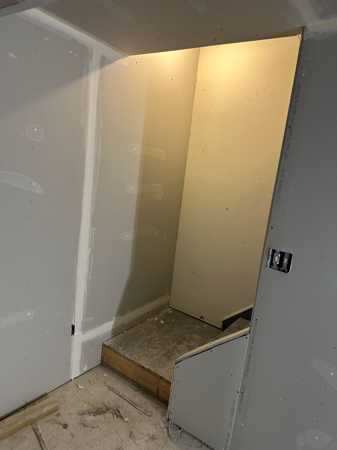 A small, unfinished stairway with drywall and a single light illuminating the space.