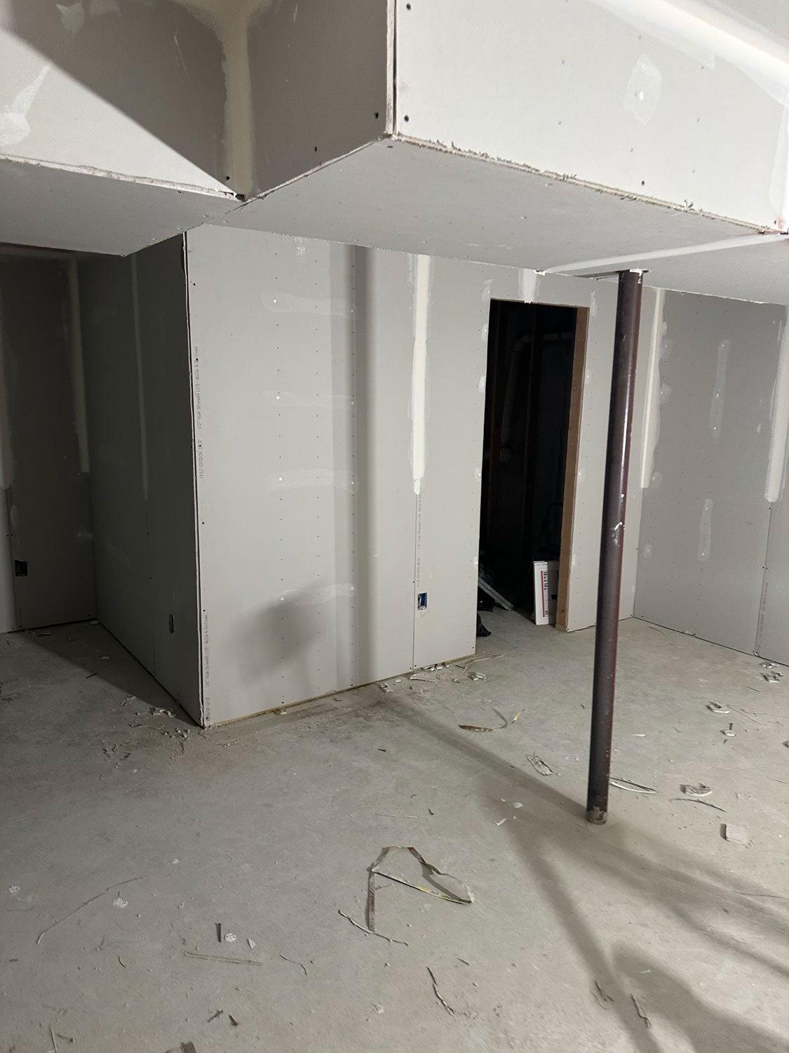 Unfinished basement with drywall installation, exposed studs, and construction debris on the concrete floor.