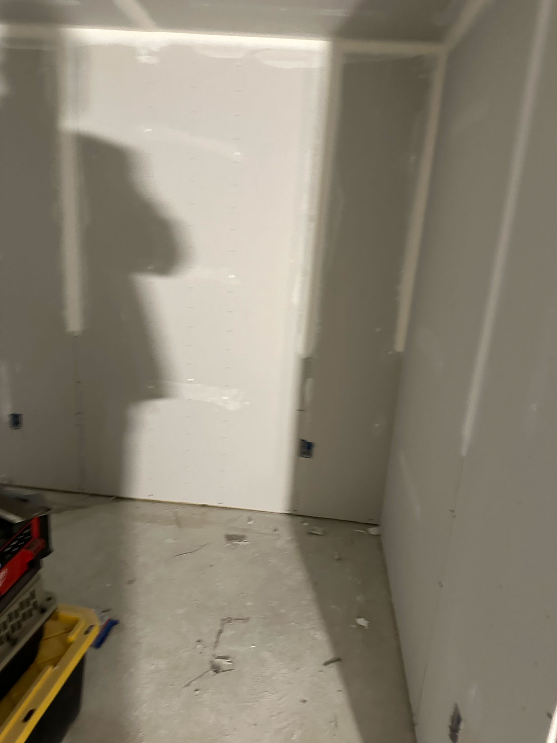 Unfinished drywall room under construction with tools and a shadow on the wall.