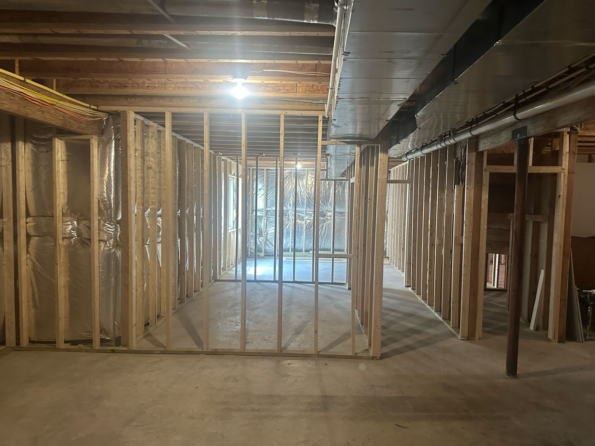 Unfinished basement with exposed framing, ceiling beams, and concrete floor, under construction.
