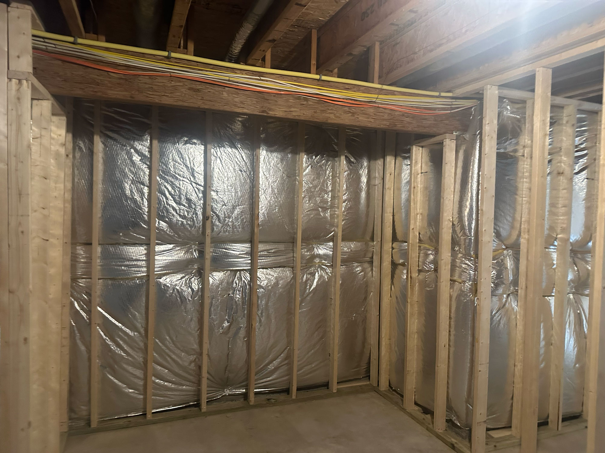 Unfinished basement with exposed wooden framing, insulation, and electrical wires along the ceiling.