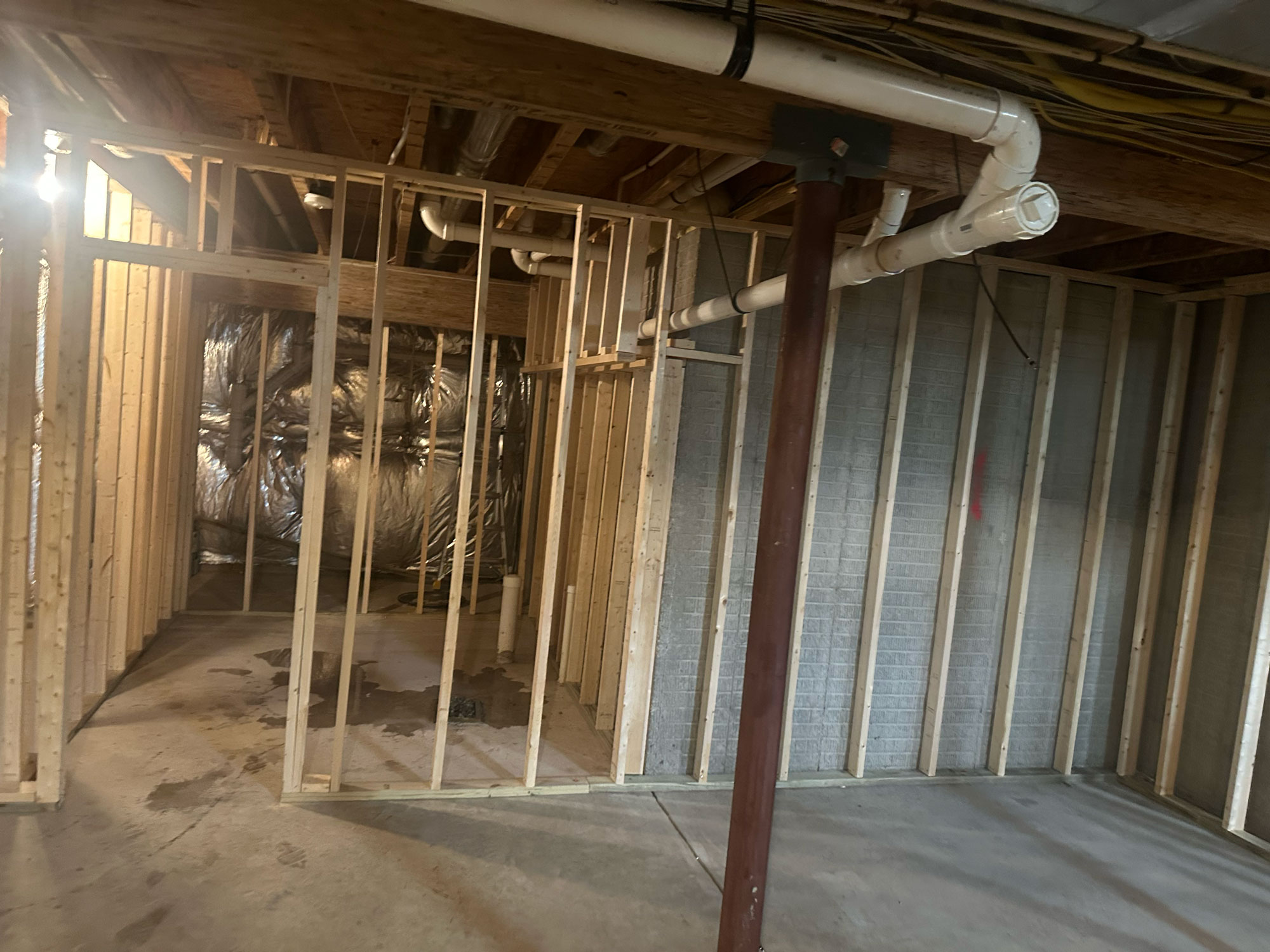 Partially finished basement with exposed framing, pipes, and insulation visible on the back wall.