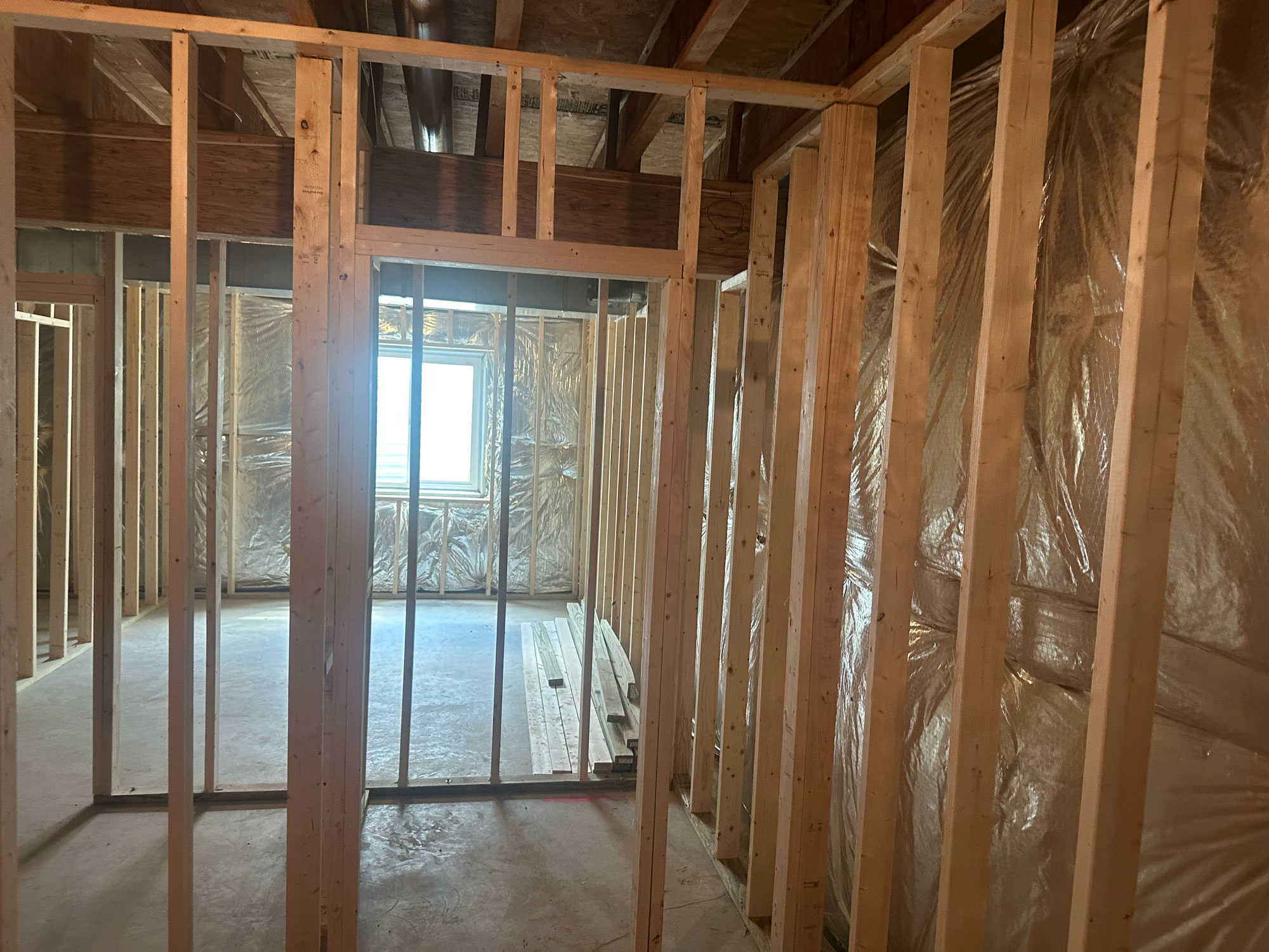 Wood framing and insulation in a house under construction, with a window letting in natural light.