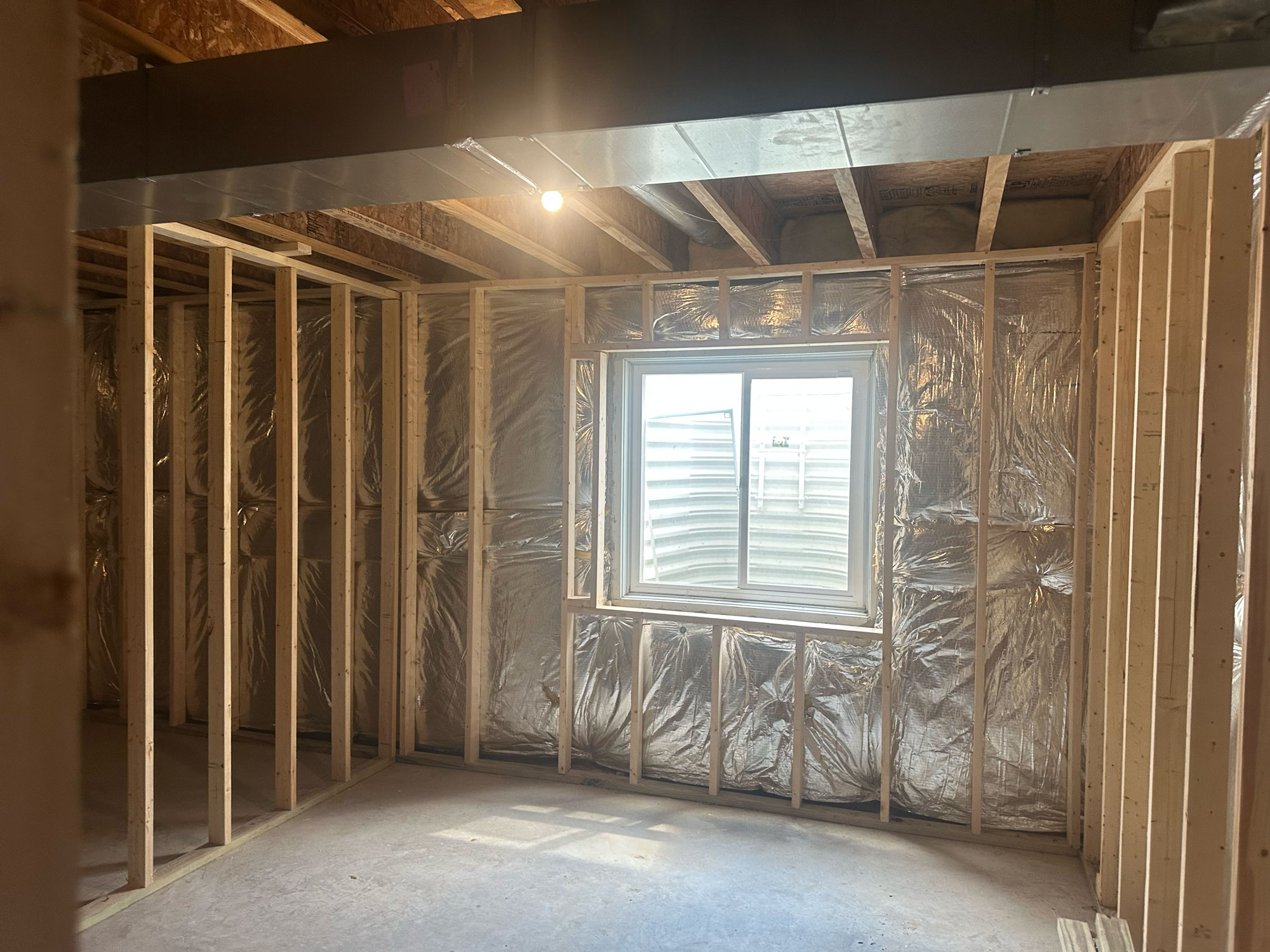 Wood framing and insulation in a basement room under construction, with a window letting in natural light.