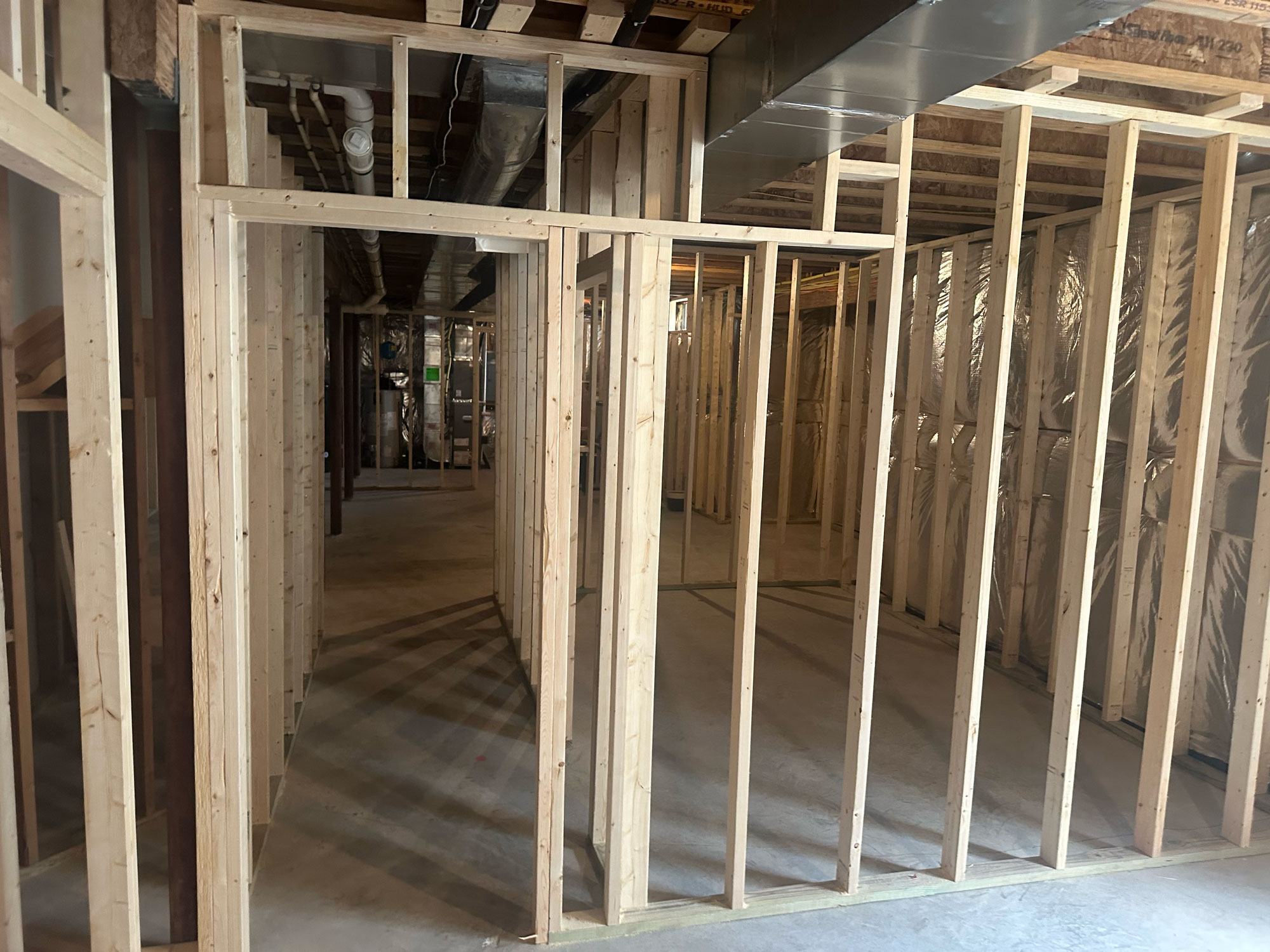 Unfinished basement with wood framing, exposed ceiling beams, and concrete floor under construction.