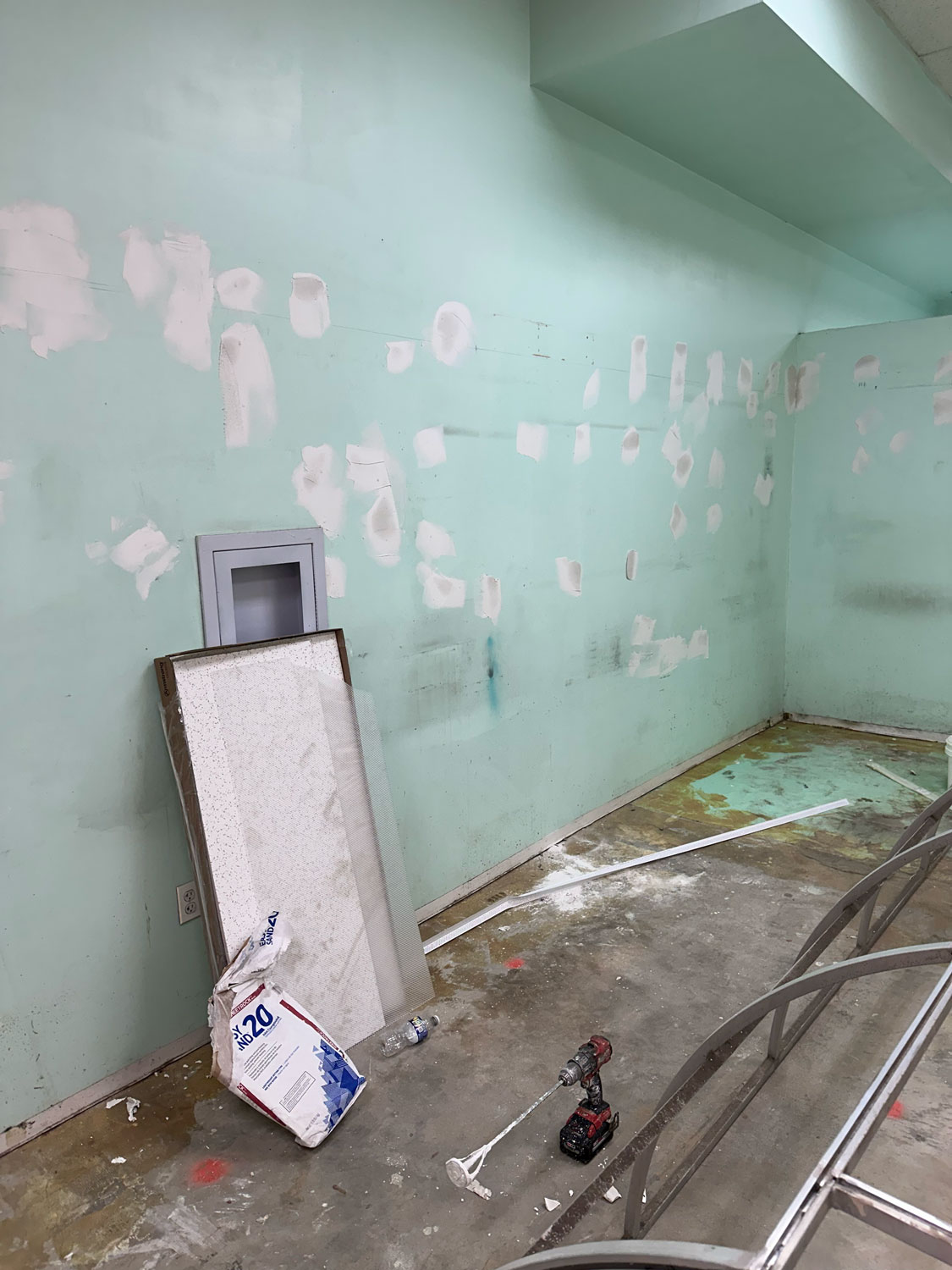 A room with patched walls, tools, debris, and construction materials scattered on the floor.