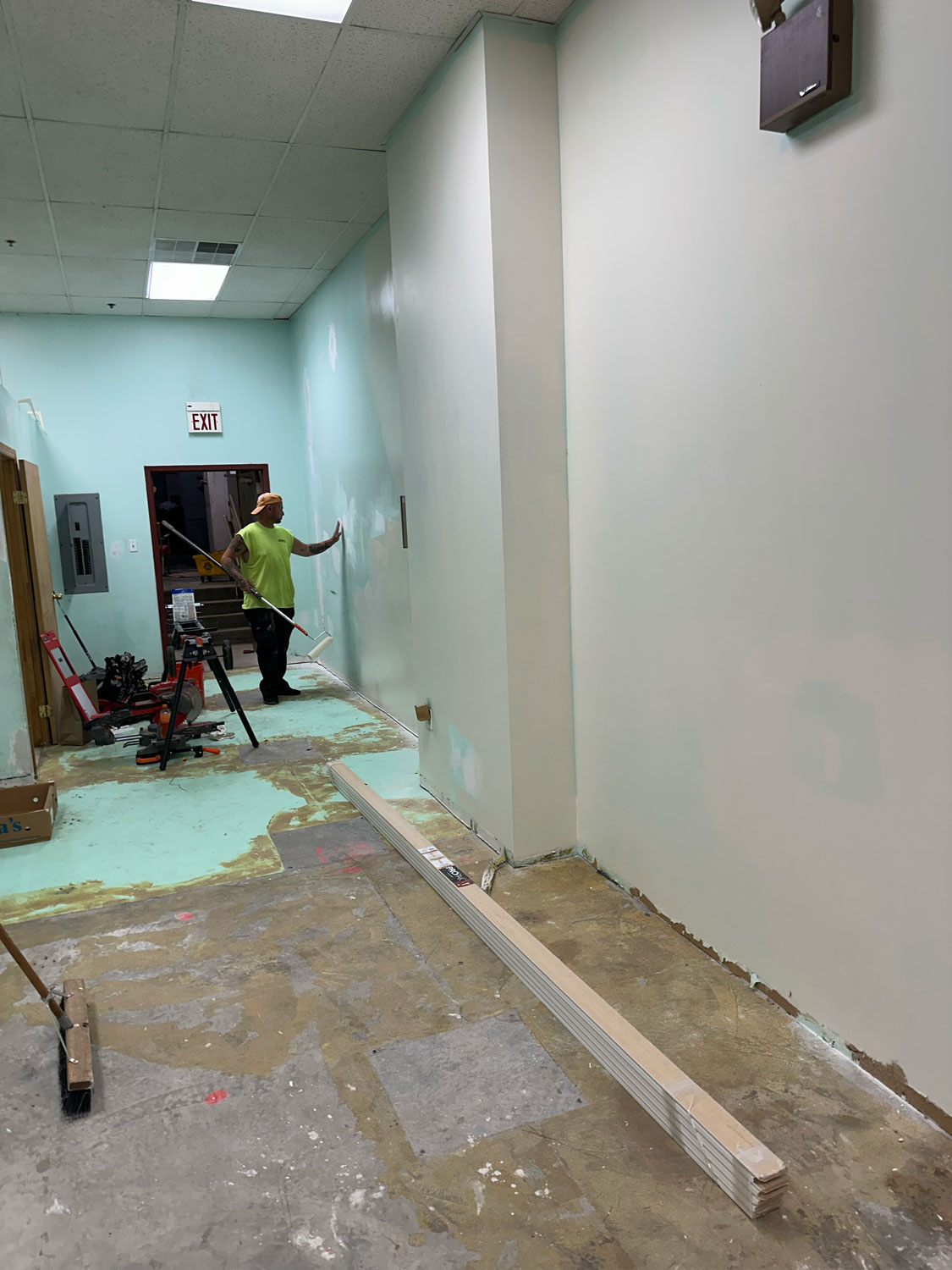 Person painting a wall in a hallway under renovation, with tools and materials on the floor.