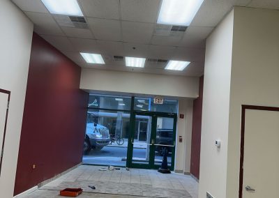 Empty storefront interior with red and white walls, tile floor, and glass doors facing a street with parked cars.