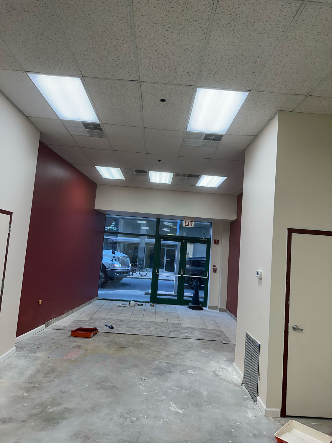Empty storefront interior with red and white walls, tile floor, and glass doors facing a street with parked cars.