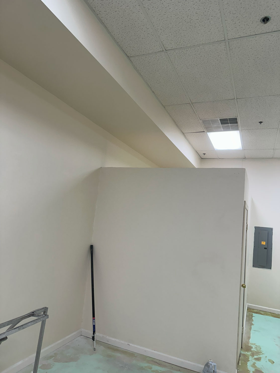 A partially painted room with unfinished floors, white walls, and a mop leaning in the corner.