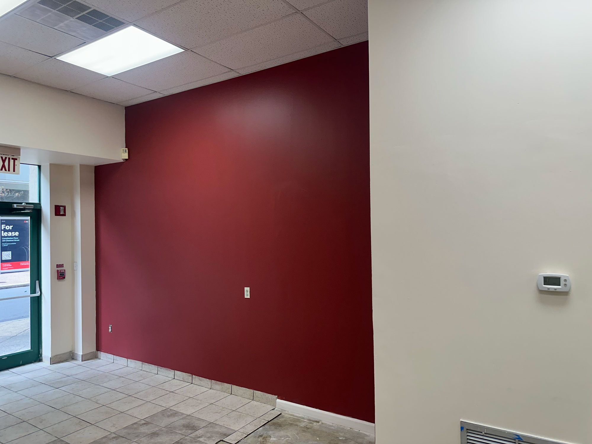 Interior wall painted dark red next to cream-colored walls, with tile flooring and partial view of a glass exit door.