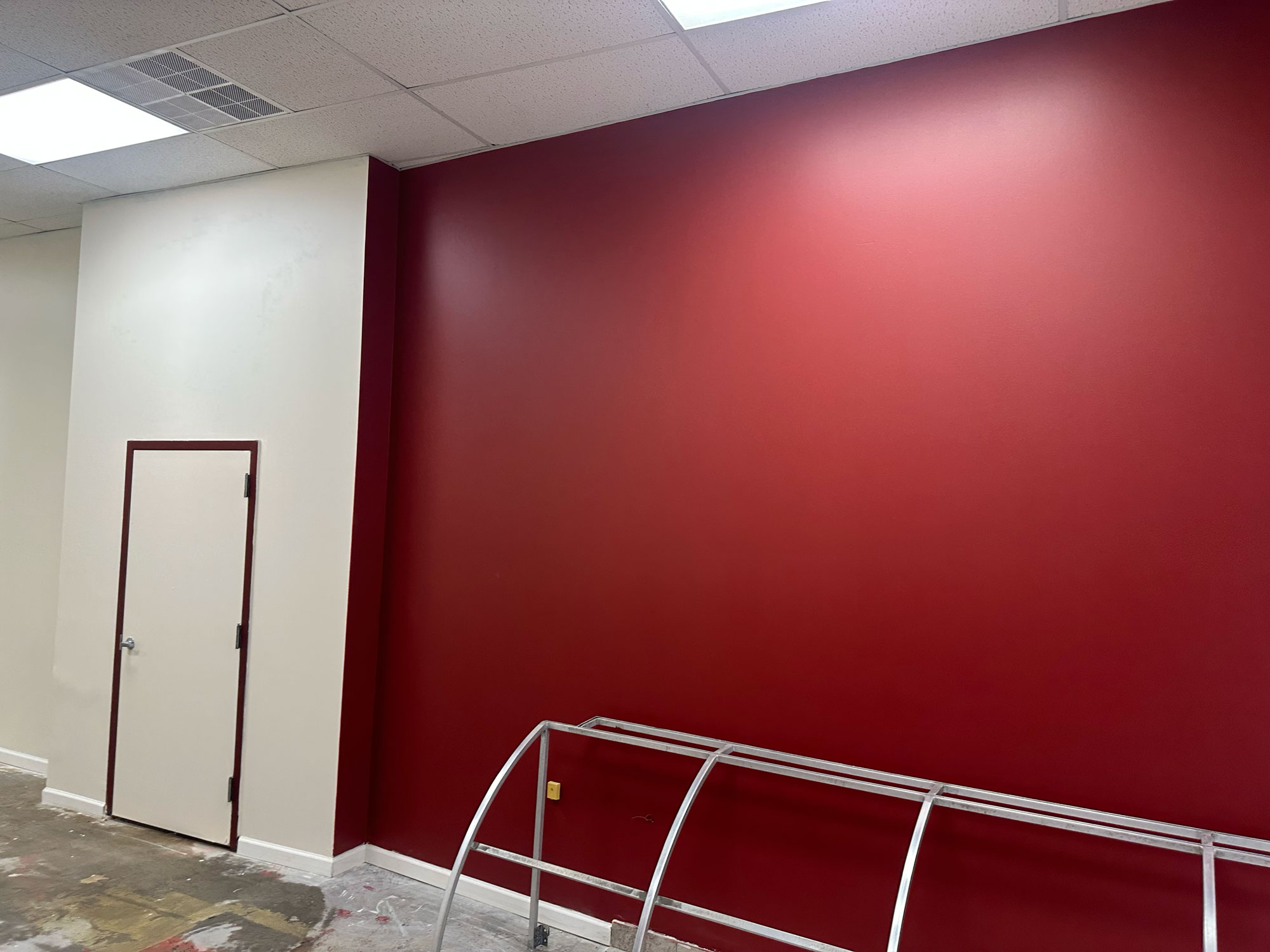 A room with a white door, beige wall, large red accent wall, and a metal frame on the floor.