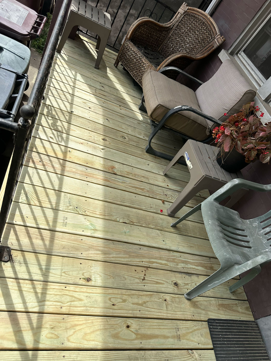 A small porch with new wooden decking, chairs, a bench, and a potted plant with red flowers.