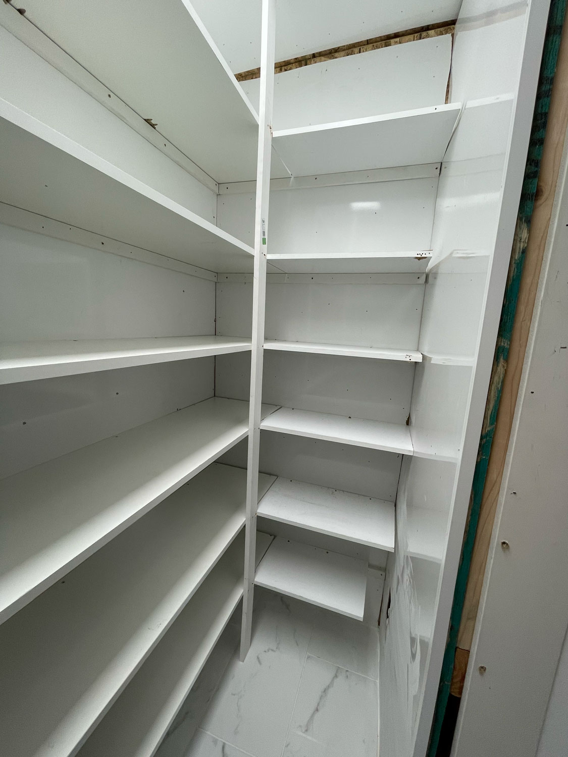 White empty pantry shelves in a small, freshly finished room with clean, glossy surfaces.