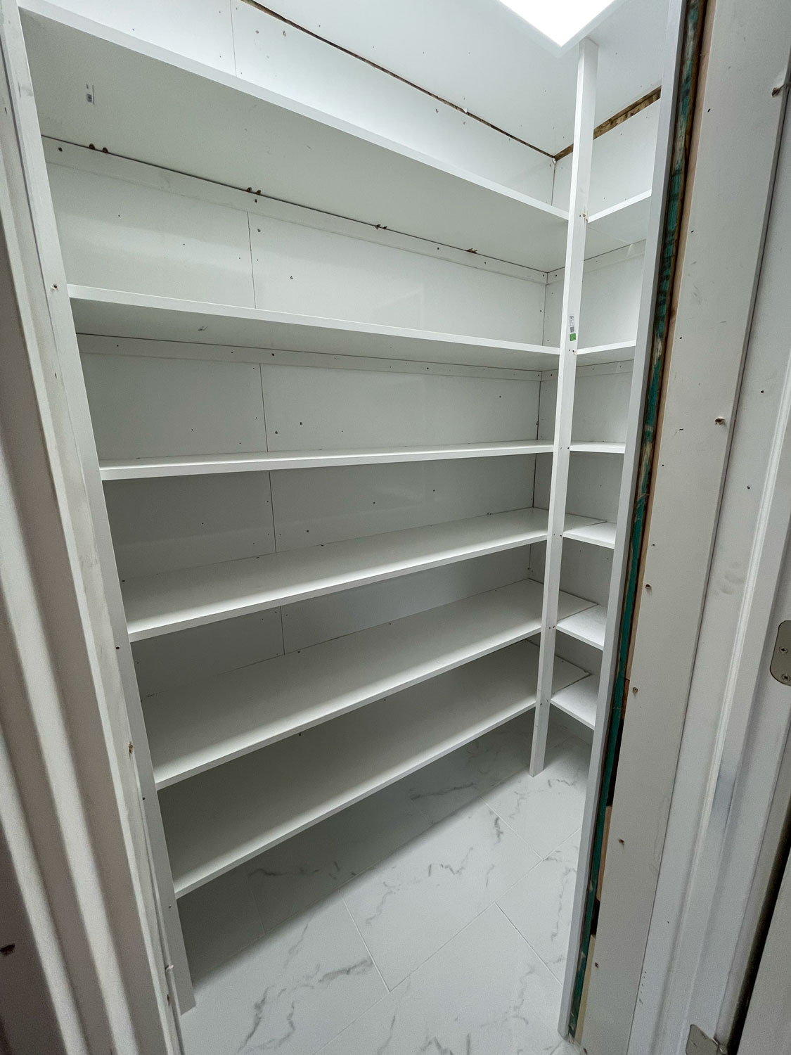 Empty white walk-in pantry with multiple shelves and a marble-patterned floor, viewed from the doorway.