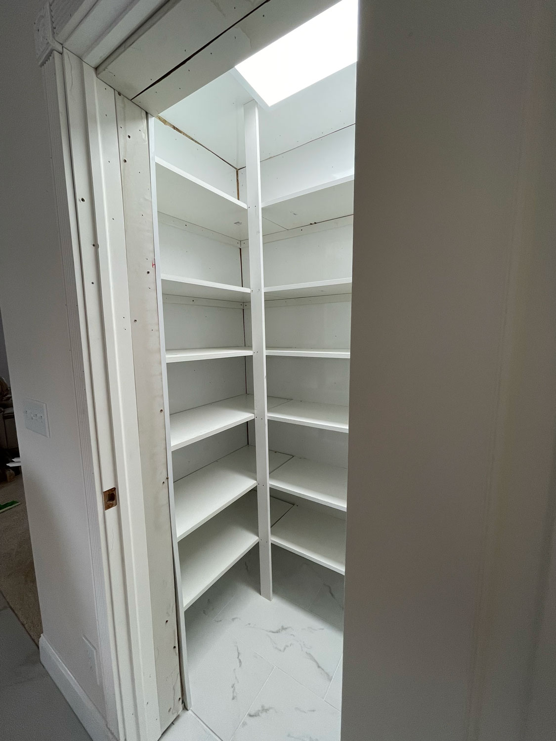 White walk-in pantry with empty shelves and a skylight above, viewed from the doorway.