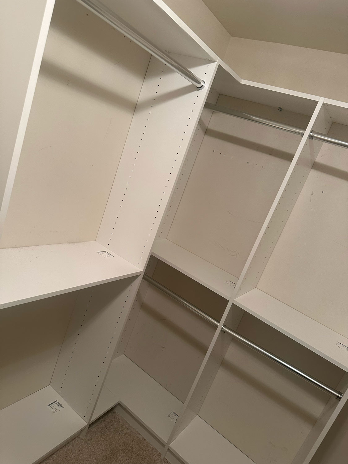 Empty white walk-in closet with shelves and metal hanging rods, viewed from an angle.
