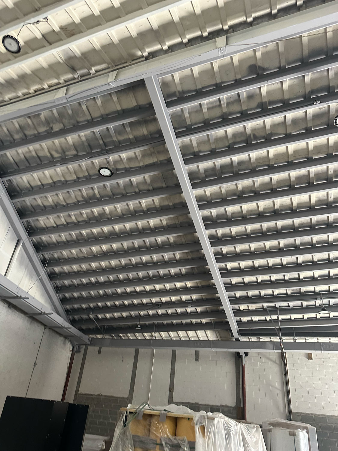 Exposed metal ceiling beams and roof panels in an unfinished industrial or warehouse space.