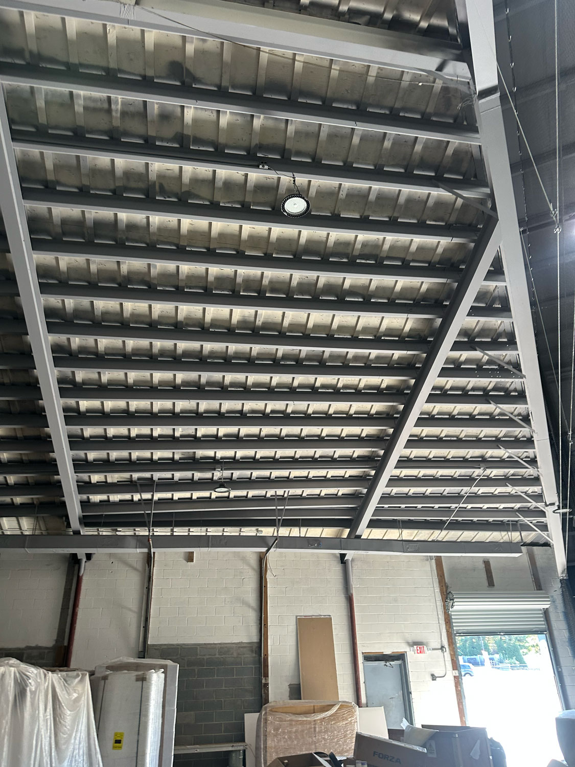 Industrial warehouse ceiling with exposed metal beams and various materials stacked below.