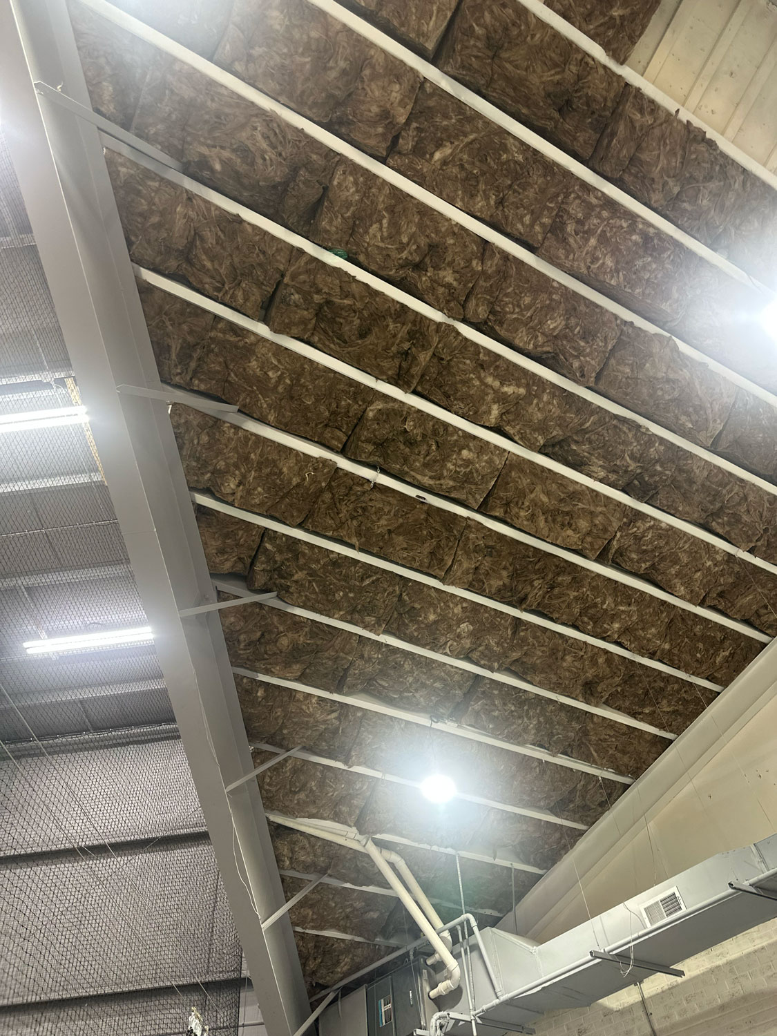 Exposed ceiling with visible insulation and beams in an industrial building with pipes and vents.