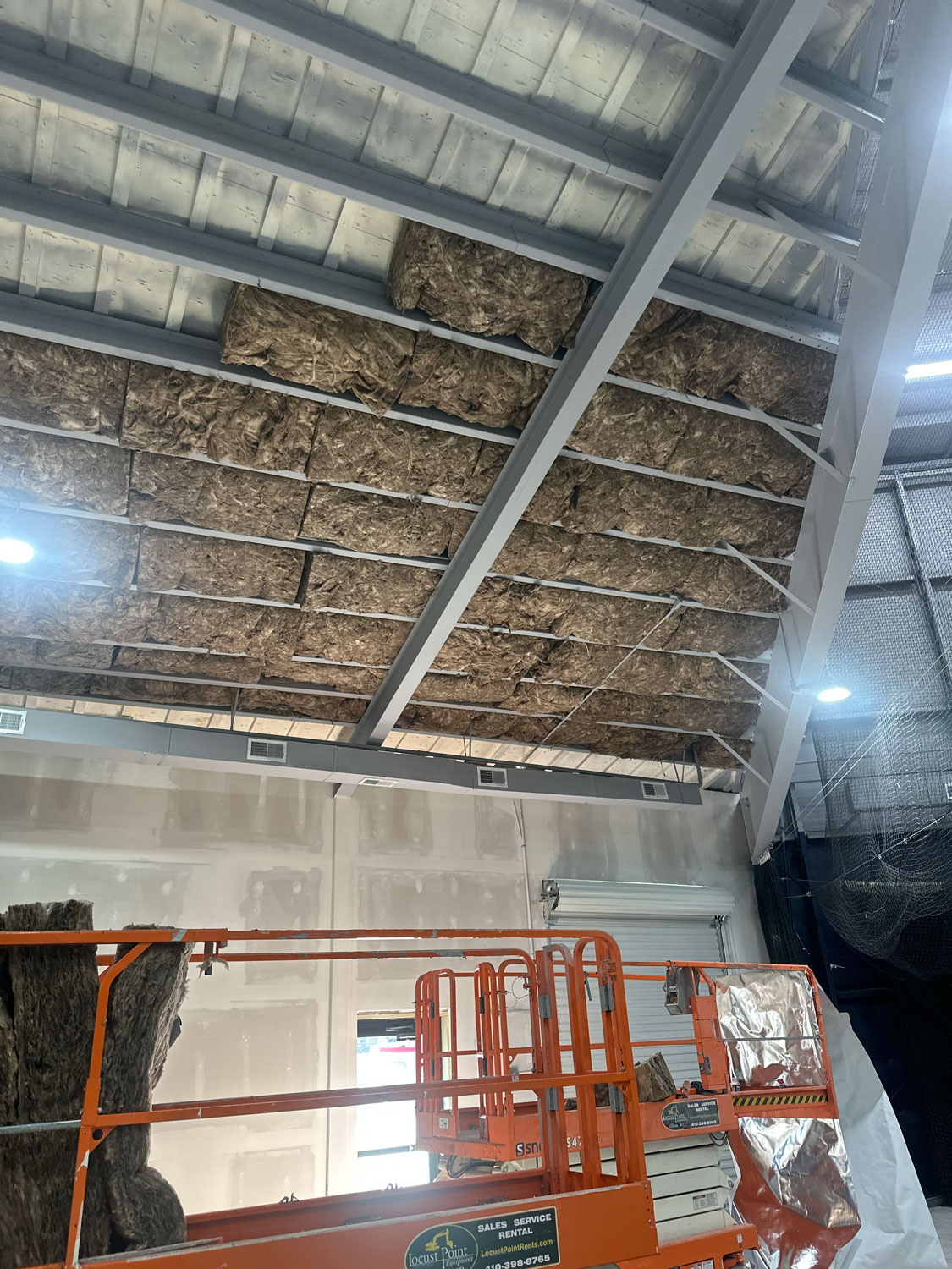 Large sheets of insulation being installed on a high, angled ceiling inside a building under construction.