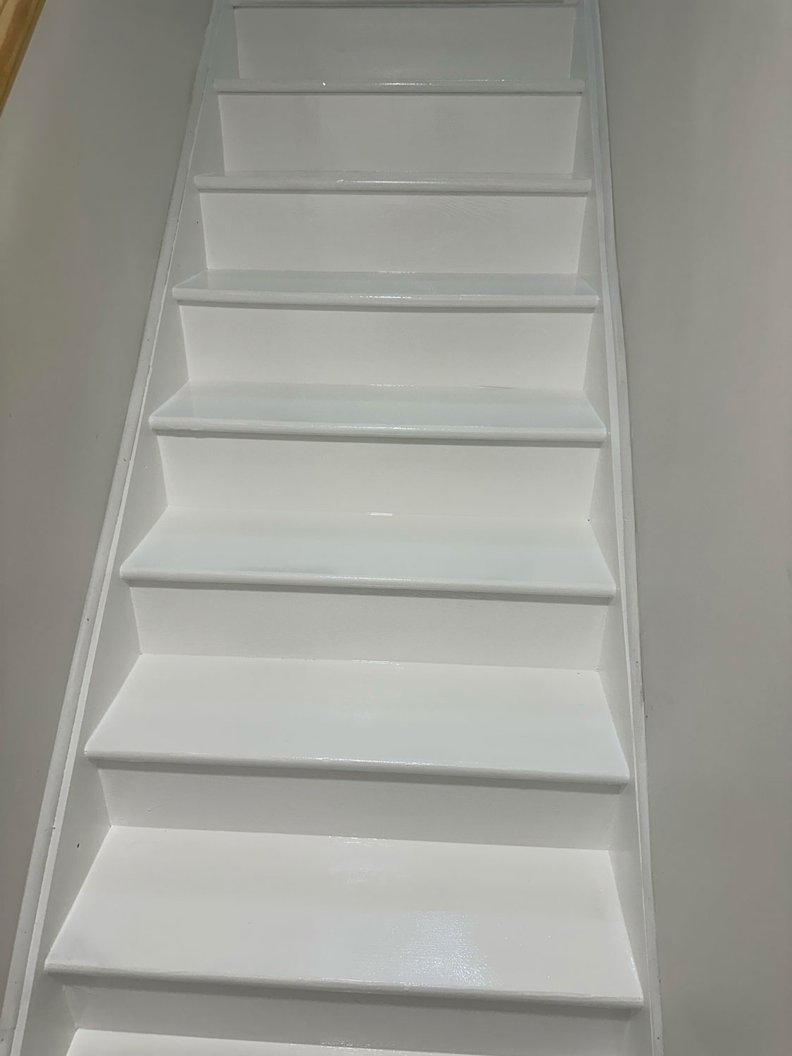 White-painted staircase with clean, glossy steps, viewed from the bottom looking upward.