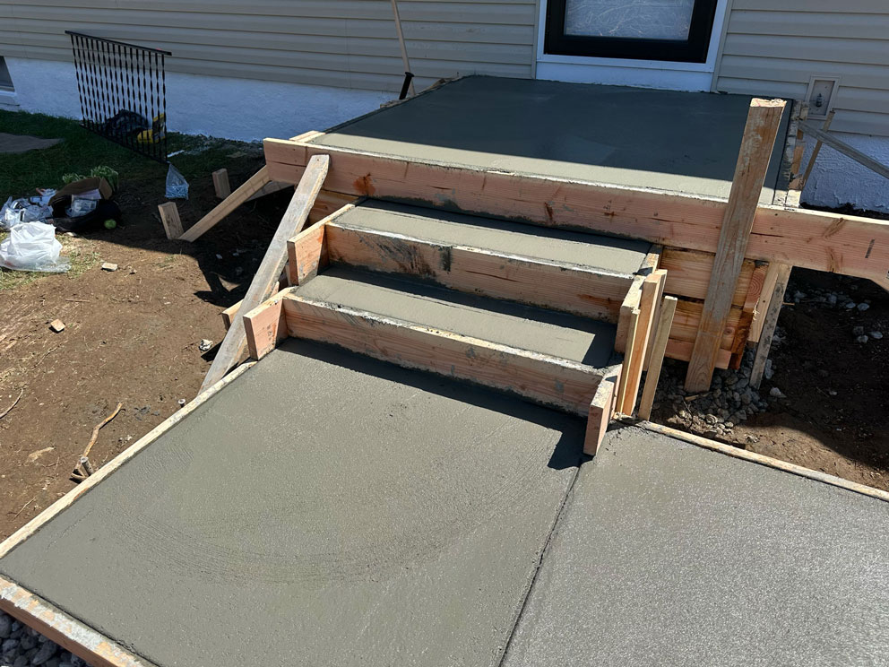 Freshly poured concrete steps and landing with wooden framing, leading to a door of a house.