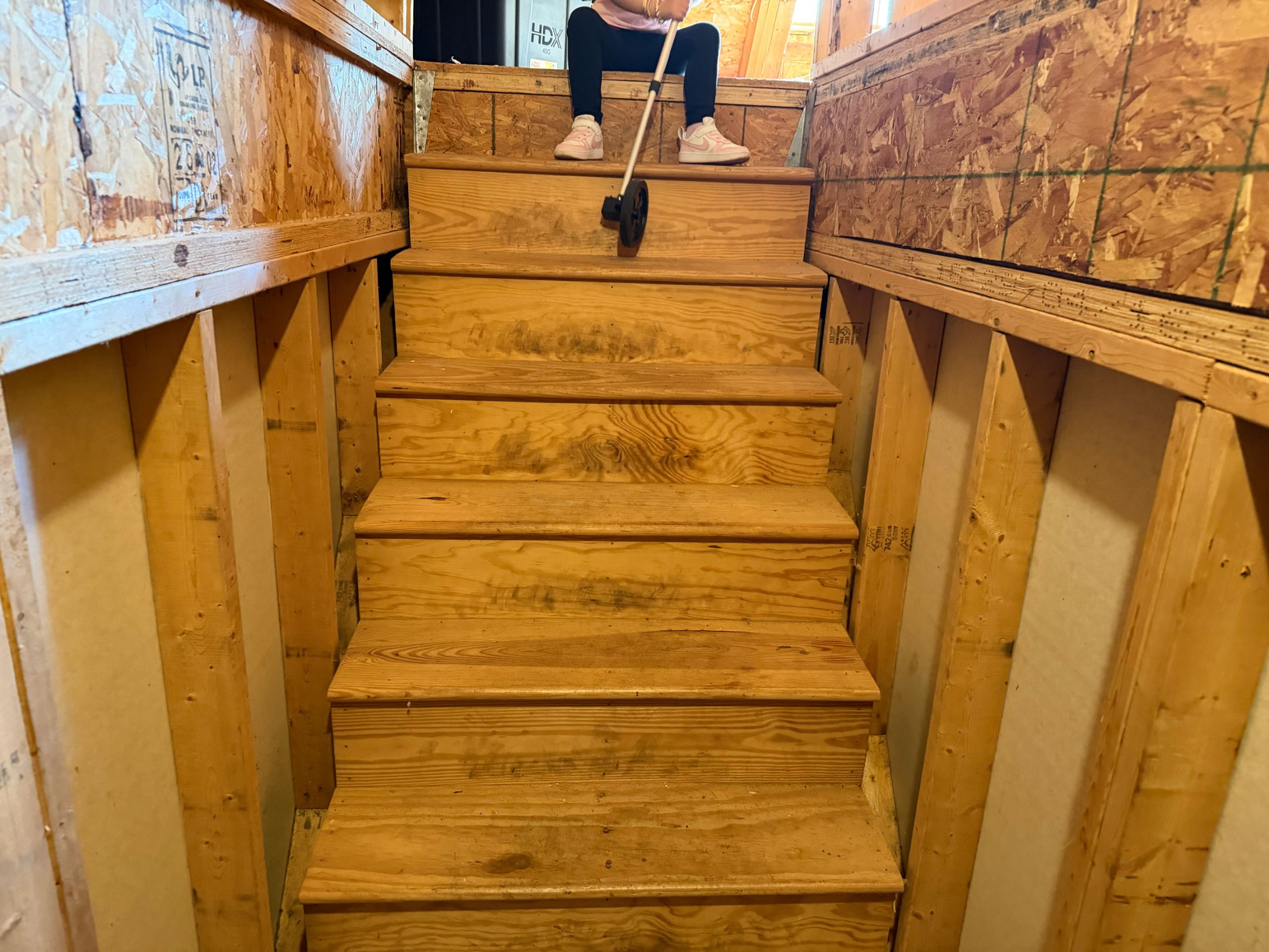 Child sitting at the top of unfinished wooden stairs in a construction area, holding a toy car on a string.