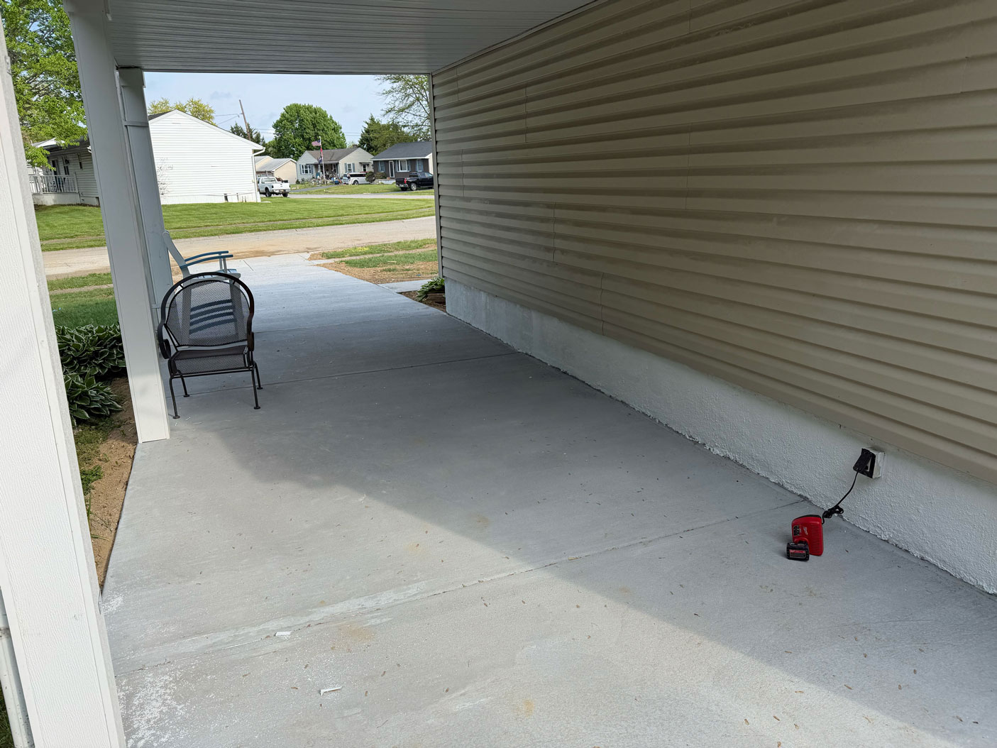 Concrete patio with two chairs, a red object near an outlet, and houses visible in the background.