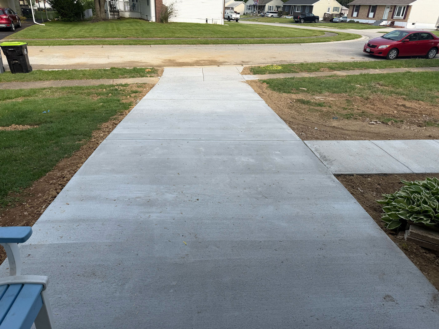 Freshly poured concrete sidewalk leading to a street, with grass and houses on either side.
