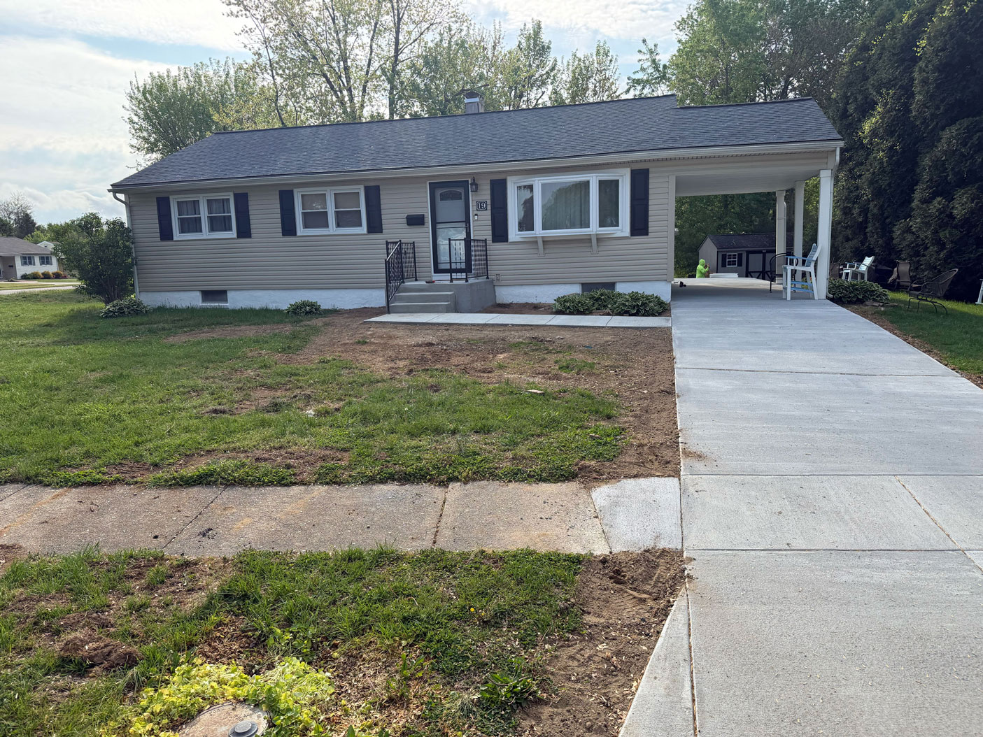 Single-story beige house with a new concrete driveway and patchy grass in the front yard.
