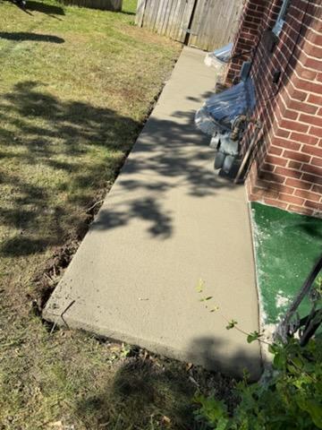 Freshly poured concrete sidewalk next to a brick house with grass and shadows nearby.